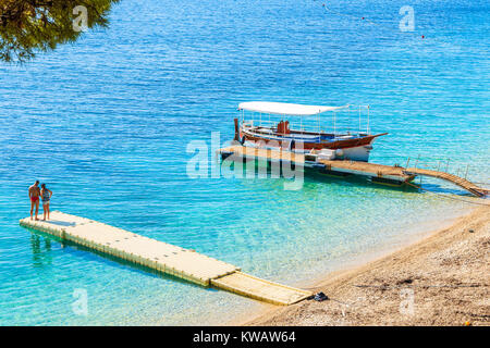 Nicht identifizierte Junge paar Leute stehen auf Pier am berühmten Strand Zlatni Rat mit schönen Meer Wasser in Bol, Insel Brac, Kroatien Stockfoto