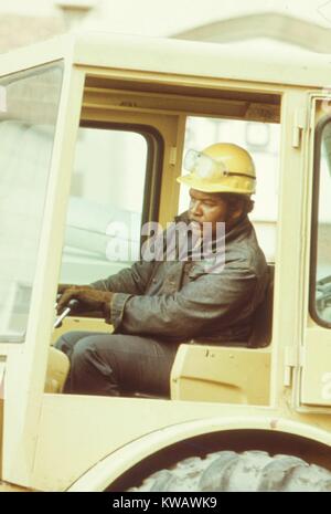 Ein Bauarbeiter in gelb Sicherheit hat die Kupplungen der Zahnräder innerhalb einer Planierraupe vor Ort in der South Side von Chicago, Illinois, 1973. Mit freundlicher Genehmigung der nationalen Archive. Stockfoto