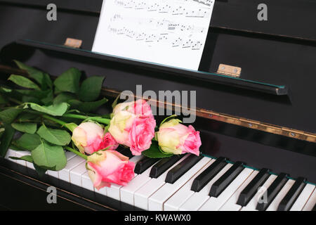 Ein Blumenstrauß aus Rosen und Noten auf der Tastatur. Das Konzept der eine musikalische Ausbildung und Konzerte. Stockfoto