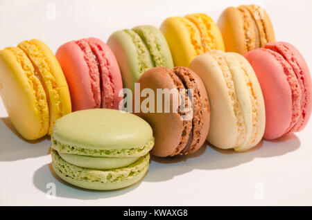 Neun macarons in verschiedenen Farben aufgereiht auf einem weißen Hintergrund Stockfoto