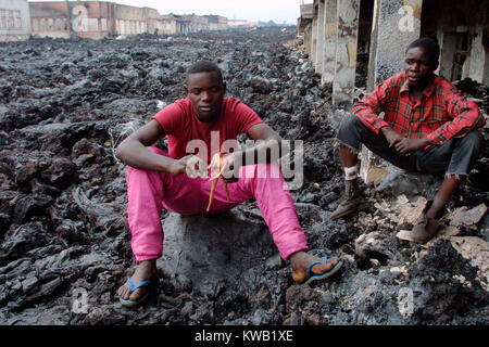 Wenn der Nyriragongo Vulkan auf 18/01/2002 ausbrach, Lava floss in Goma in der Demokratischen Republik Kongo, zerstören ein Drittel der Stadt. Diese Teenager sitzt auf der Kühlung Lava mit einem gebrochenen Puppe, während hinter ihm eine der wichtigsten Straßen der Stadt in Ruinen liegt. Stockfoto