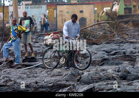 Wenn der Nyriragongo Vulkan auf 18/01/2002 ausbrach, Lava floss in Goma in der Demokratischen Republik Kongo, zerstören ein Drittel der Stadt. Da die Lava gekühlt die meisten Einwohner der Stadt zurück. Dieser Mann Räder sein Fahrrad über den Lavastrom. Stockfoto