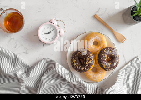 Blick von oben auf die Kaffeetasse mit Donut und die Uhr auf dem Tisch. Frühstück am Morgen. Stockfoto