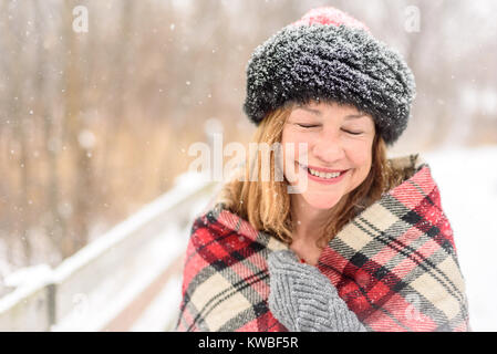 Lächelnde Frau draußen genießen Sie frischen Schneefall in Holz gebündelt Stockfoto