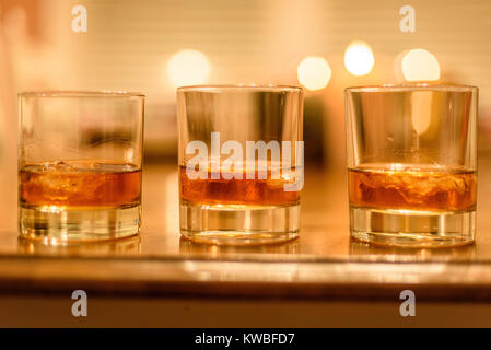 Nahaufnahme der Bourbon Whiskey Gläser mit Eis bis auf Holz Tisch mit Kerzen im Hintergrund gefüttert Stockfoto