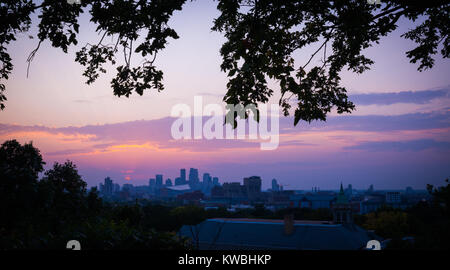 sunset with the minneapolis minnesota skyline framed with leaves and branches. sky is pink, blue, orange and purple with low horizon of skyscrapers. Stockfoto