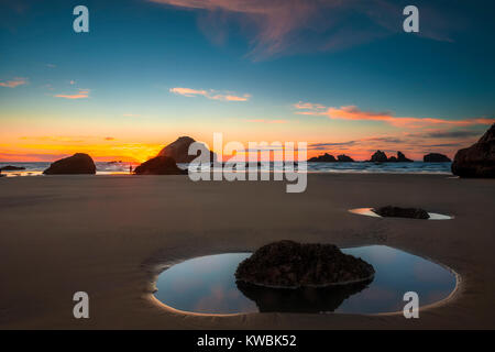 Tide pool bei Ebbe auf dem Oregon Bandon Strand bei Sonnenuntergang. Ein einsamer Mann steht mit Blick auf die Szene. Stockfoto