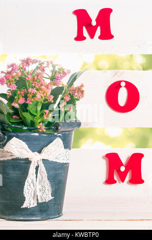 Das Wort Mama mit rotem Papier geschrieben und zu einem weißen Zaun und Blumen in einem Blumentopf in Form einer Schaufel festgesteckt, mit Spitze Band und Bogen. Stockfoto