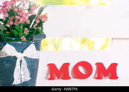 Muttertag Grußkarte Idee mit dem Wort Mama mit rotem Papier Buchstaben auf weißem Zaun lehnte geschrieben, in der Nähe einer alten Schaufel voll mit Blumen. Stockfoto