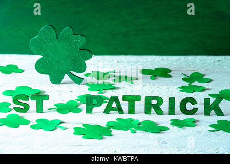 Saint Patrick Worte mit grünem Holz- buchstaben und einem großen grünen Shamrock in der Rückseite geschrieben, umgeben von Papier Klee, auf einer hölzernen Hintergrund. Stockfoto