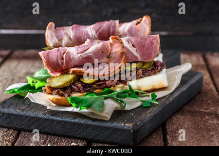 Delicius Sandwiches mit geräuchertem Schweinefleisch, Gurken und Zwiebeln auf einem schwarzen Brett. Stockfoto