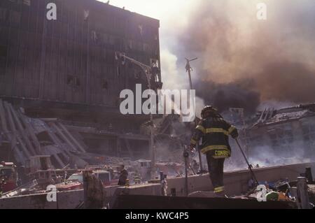Feuerwehrleute unter Trümmern nach dem 11. September Terroranschlag auf World Trade Center. Foto zeigt die noch stehende WTC 6 und die zerstörten nördlichen Fußgängerbrücke über West Side Highway (West St.). Im Foto ist oben rechts der Rauch aus dem brennenden Haufen von eingestürzten WTC 1 (Nordturm). New York City, 11. September 2001. (BSLOC 2015 2 46) Stockfoto