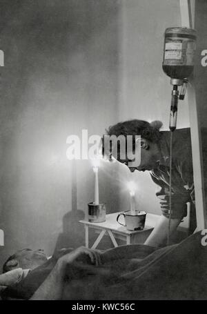 Amerikanische Armee Krankenschwester an Kerze am Bett des verletzten Soldaten in Frankreich während des Zweiten Weltkrieges 2. Er erhält eine Transfusion an einer Front Krankenhaus zeigt eine große Verlieren von Blut aus der Wunde. Jan 23, 1945. (BSLOC 2015 13 83) Stockfoto