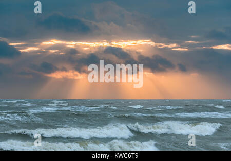 Niedrige Sonne durch die Wolken mit Sonnenstrahlen Übersicht über eine rauhe See im Winter in Großbritannien versteckt. Stockfoto