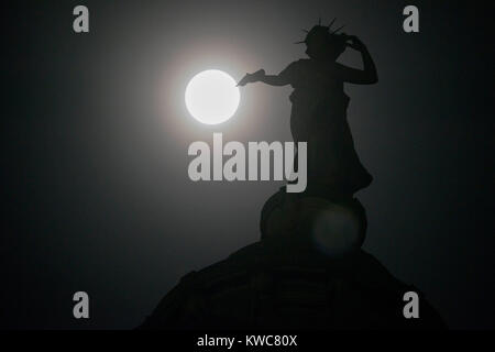 Das neue Jahr supermoon - auch als Wolf Mond - dargestellt in vollen Zügen mitten in der Nacht des 2. Januar hinter Bronze Thomas Clapperton Statue namens Literatur, die auf der Oberseite des Mitchell Library, Glasgow, Schottland sitzt bekannt. Stockfoto