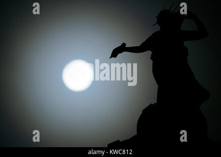 Das neue Jahr supermoon - auch als Wolf Mond - dargestellt in vollen Zügen mitten in der Nacht des 2. Januar hinter Bronze Thomas Clapperton Statue namens Literatur, die auf der Oberseite des Mitchell Library, Glasgow, Schottland sitzt bekannt. Stockfoto