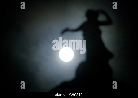 Das neue Jahr supermoon - auch als Wolf Mond - dargestellt in vollen Zügen mitten in der Nacht des 2. Januar hinter Bronze Thomas Clapperton Statue namens Literatur, die auf der Oberseite des Mitchell Library, Glasgow, Schottland sitzt bekannt. Stockfoto