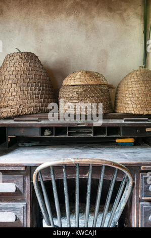 Die Lost Gardens of Heligan, Cornwall, UK. Alte Stroh Bienenstöcke (skeps) auf einem Schreibtisch im Büro Der alte Gärtner Stockfoto