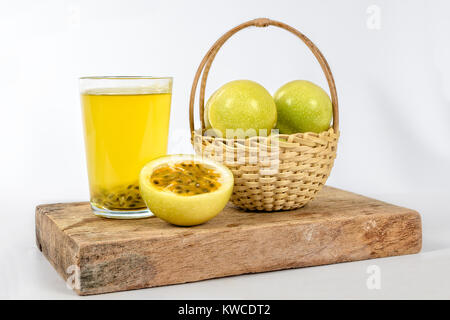 Ein Glas Passionsfruchtsaft, ein Korb mit einer Gruppe von Leidenschaft, Früchte und eine Hälfte Maracuja, all dies auf einem Stück Holz. Stockfoto