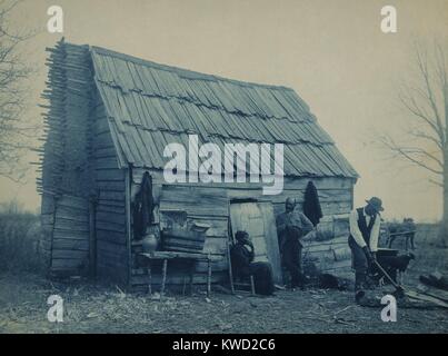 African American man hackt Holz außen eine Kabine, vermutlich die Heimat der Paar mittleren Alters in der Nähe. Der Baum ist Tragen von Blättern, und Brennholz wird gebraucht werden. 1899-1900 Foto von Frances Benjamin Johnston, 1899-1900, der südlichen Architektur fotografiert, afrikanische Amerikaner und Indianer an der Wende des 20. Jahrhunderts (BSLOC 2017 20 127) Stockfoto