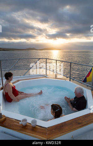 Galapagos Reisen - Touristen in einem Whirlpool auf dem Kreuzfahrtschiff beobachten Sonnenuntergang über der Insel Floreana, Galapagos, Ecuador Südamerika Stockfoto