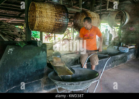 Thailändische Arbeiter entfernen verdampft Kokosnuss Zucker sap-Sirup von heißen Pfannen bei Kokosnuss Zucker Plantation, Tambon Kradangnga, Samut Songkhram, Thailand. Stockfoto