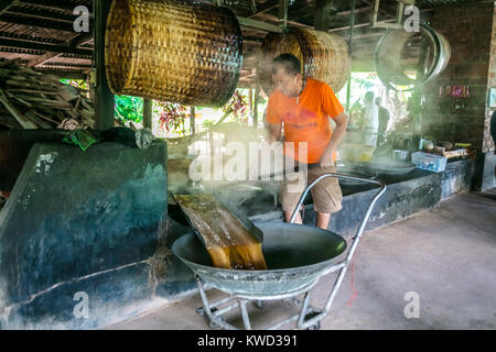 Thailändische Arbeiter entfernen verdampft Kokosnuss Zucker sap-Sirup von heißen Pfannen bei Kokosnuss Zucker Plantation, Tambon Kradangnga, Samut Songkhram, Thailand. Stockfoto