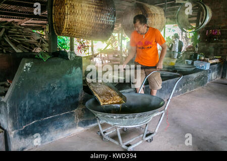 Thailändische Arbeiter entfernen verdampft Kokosnuss Zucker sap-Sirup von heißen Pfannen bei Kokosnuss Zucker Plantation, Tambon Kradangnga, Samut Songkhram, Thailand. Stockfoto