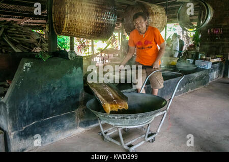 Thailändische Arbeiter entfernen verdampft Kokosnuss Zucker sap-Sirup von heißen Pfannen bei Kokosnuss Zucker Plantation, Tambon Kradangnga, Samut Songkhram, Thailand. Stockfoto