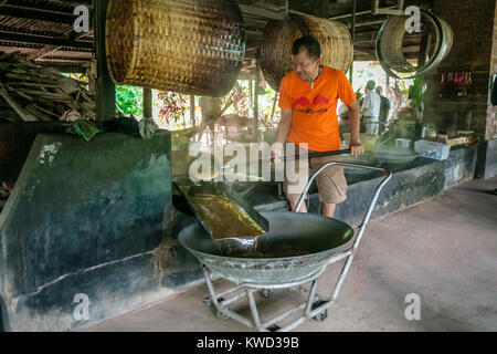 Thailändische Arbeiter entfernen verdampft Kokosnuss Zucker sap-Sirup von heißen Pfannen bei Kokosnuss Zucker Plantation, Tambon Kradangnga, Samut Songkhram, Thailand. Stockfoto