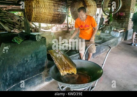 Thailändische Arbeiter entfernen verdampft Kokosnuss Zucker sap-Sirup von heißen Pfannen bei Kokosnuss Zucker Plantation, Tambon Kradangnga, Samut Songkhram, Thailand. Stockfoto