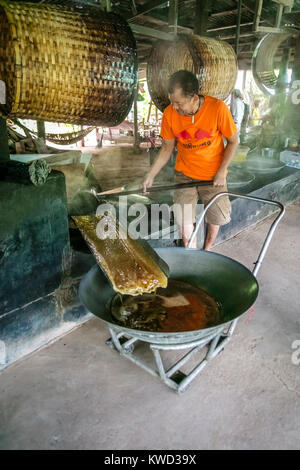 Thailändische Arbeiter entfernen verdampft Kokosnuss Zucker sap-Sirup von heißen Pfannen bei Kokosnuss Zucker Plantation, Tambon Kradangnga, Samut Songkhram, Thailand. Stockfoto