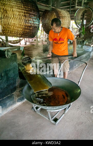 Thailändische Arbeiter entfernen verdampft Kokosnuss Zucker sap-Sirup von heißen Pfannen bei Kokosnuss Zucker Plantation, Tambon Kradangnga, Samut Songkhram, Thailand. Stockfoto