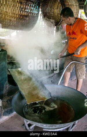 Thailändische Arbeiter entfernen verdampft Kokosnuss Zucker sap-Sirup von heißen Pfannen bei Kokosnuss Zucker Plantation, Tambon Kradangnga, Samut Songkhram, Thailand. Stockfoto