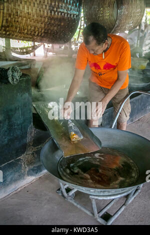 Thailändische Arbeiter entfernen verdampft Kokosnuss Zucker sap-Sirup von heißen Pfannen bei Kokosnuss Zucker Plantation, Tambon Kradangnga, Samut Songkhram, Thailand. Stockfoto