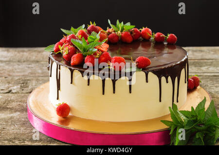 Schönen Kuchen mit schwarzer Schokolade mit Erdbeeren und Minze closeup auf einem Holztisch auf schwarzem Hintergrund Stockfoto