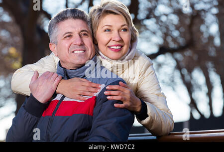 Mann und Frau umarmen einander sitzen auf einer Parkbank Stockfoto