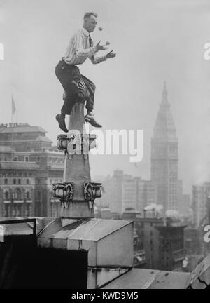 "Menschliche Fliegen 'John' Jammie "Reynolds jongliert während Balancing auf einem Dach Dekoration in New York City. In der Ferne ist der New York Life Building am Madison Square Park. Ca. 1915-1920. (BSLOC 2015 17 169) Stockfoto