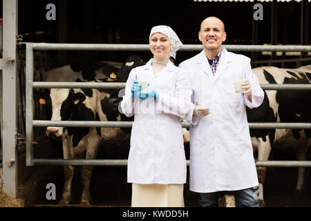 Glücklich der Mann und die Frau Tierärzte glücklich in der Nähe stehen Kühe auf Bauernhof mit Glas Milch Stockfoto