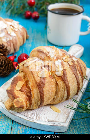 Croissants mit Mandelflocken, Kaffeetasse auf einem blauen Hintergrund aus Holz. Frühstück. Traditionelles französisches Gebäck. Stockfoto