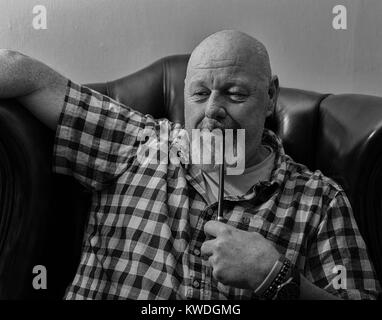 Ein reifer Mann in einem Flügel zurück Sessel mit einem Rohr, in eine nachdenkliche Stimmung. Stockfoto