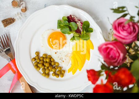 Festliche Frühstück. Rührei, grüne Erbsen und Salat, ein Strauß Rosen. Blick von oben. Valentinstag Konzept. Stockfoto