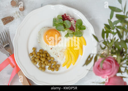 Festliche Frühstück. Rührei, grüne Erbsen und Salat, ein Strauß Rosen. Blick von oben. Valentinstag Konzept. Stockfoto