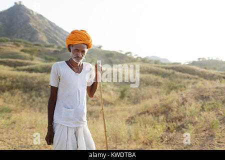 Porträt eines Kamels Händler auf seinen Stock mit seiner Herde weiden im Busch in der Nähe des jährlichen Pushkar Camel Fair, Pushkar, Rajasthan, Indien Stockfoto