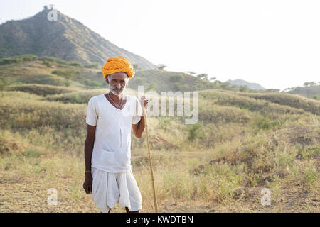 Porträt eines Kamels Händler auf seinen Stock mit seiner Herde weiden im Busch in der Nähe des jährlichen Pushkar Camel Fair, Pushkar, Rajasthan, Indien Stockfoto