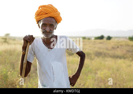 Porträt eines Kamels Händler auf seinen Stock mit seiner Herde weiden im Busch in der Nähe des jährlichen Pushkar Camel Fair, Pushkar, Rajasthan, Indien Stockfoto