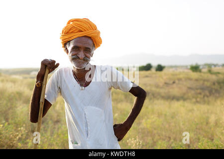 Porträt eines Kamels Händler auf seinen Stock mit seiner Herde weiden im Busch in der Nähe des jährlichen Pushkar Camel Fair, Pushkar, Rajasthan, Indien Stockfoto