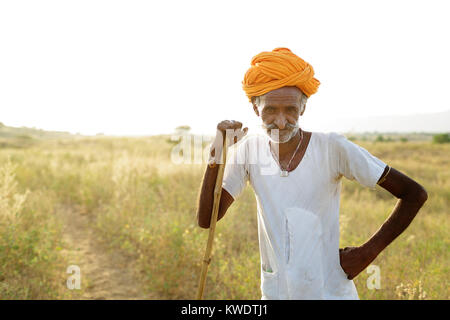 Porträt eines Kamels Händler auf seinen Stock mit seiner Herde weiden im Busch in der Nähe des jährlichen Pushkar Camel Fair, Pushkar, Rajasthan, Indien Stockfoto