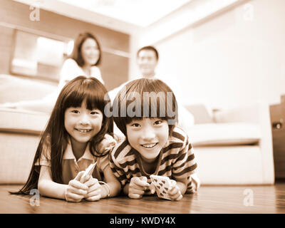 Asiatische Bruder und Schwester liegen auf der Vorderseite auf den Boden mit den Eltern im Hintergrund, Schwarz und Weiß. Stockfoto