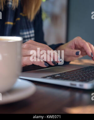 Nahaufnahme von Frau Tippen auf Laptop Tastatur mit Latte Stockfoto